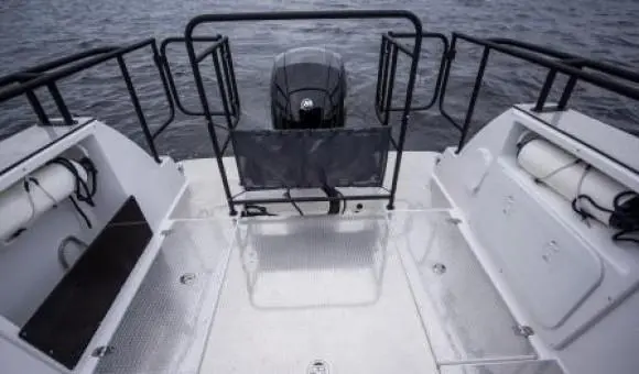 View of a boat's rear deck with a motor, handrails, and two storage compartments, set against a grey water backdrop.